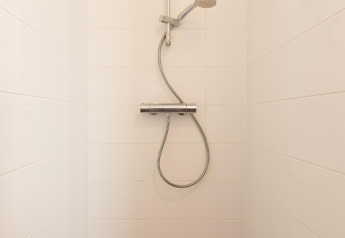 Ducha minimalista con azulejos blancos y grifo de mano en el baño de la tiny house Comfort Lodge.