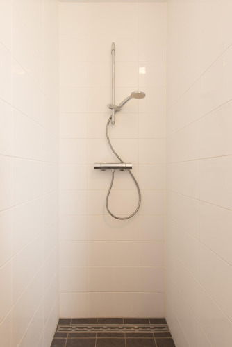 Ducha minimalista con azulejos blancos y grifo de mano en el baño de la tiny house Comfort Lodge.