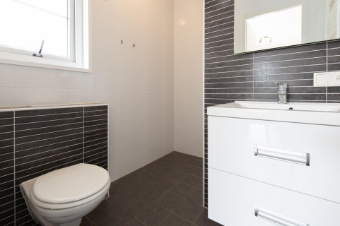 Moderne badkamer in Comfort Lodge tiny house met toilet, lavabo, spiegel en zwart-witte tegels.
