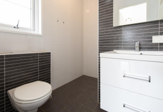 Modern bathroom in Comfort Lodge tiny house with toilet, sink cabinet, mirror, and black-white tiles.