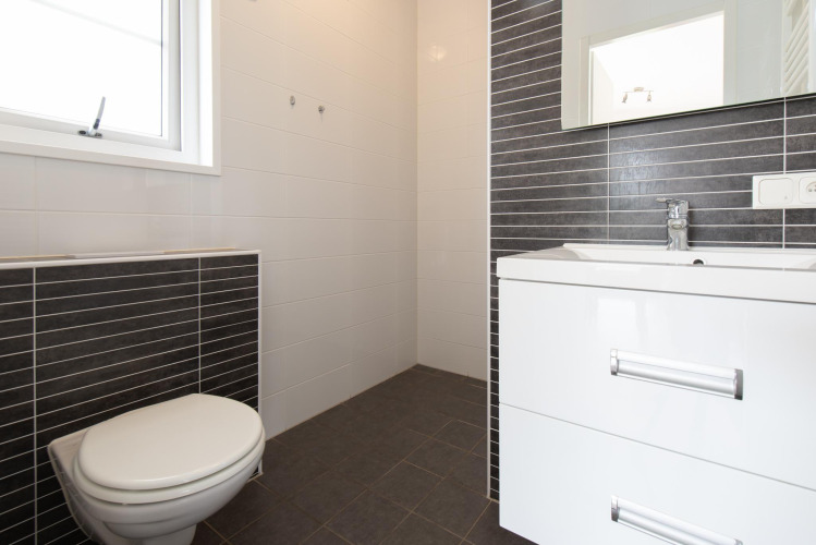 Baño moderno en una tiny house Comfort Lodge con inodoro, lavabo, espejo y azulejos blanco-negros.