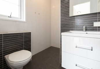 Bagno moderno nella tiny house Comfort Lodge con wc, lavabo, specchio e piastrelle bianco-nere.
