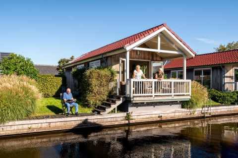 Billede af Meine Luxe lodge ved Tusken de Marren i Holland, med folk på verandaen og ved kanalen.