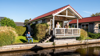Billede af Meine Luxe lodge ved Tusken de Marren i Holland, med folk på verandaen og ved kanalen.