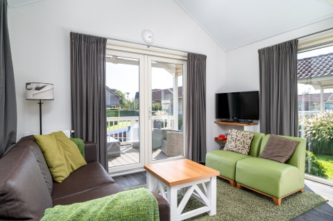 Stue i Meine Luxe lodge med grøn sofa, TV, brun sofa og udsigt til terrasse i Tusken de Marren, Holland.