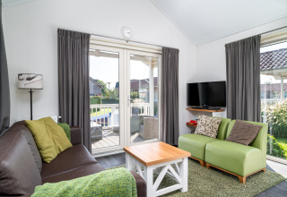 Stue i Meine Luxe lodge med grøn sofa, TV, brun sofa og udsigt til terrasse i Tusken de Marren, Holland.