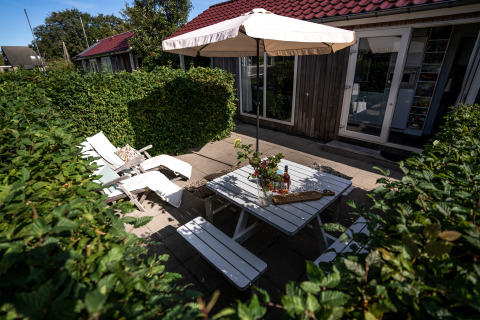 Udendørs terrasse ved Meine Luxe lodge med hvidt havemøblement og parasol i Tusken de Marren, Holland.