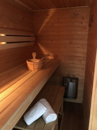 Vista interior de una sauna de madera con banco, toallas, cubo y estufa en Meine Luxe, Tusken de Marren, Países Bajos.