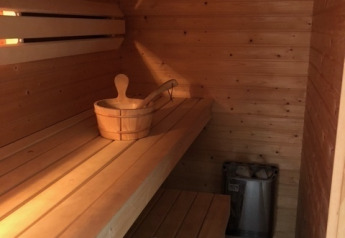 Binnenaanzicht van een houten sauna met bank, handdoeken, emmer en kachel bij Meine Luxe, Tusken de Marren, Nederland.