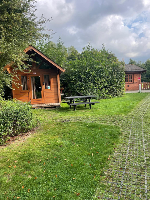 Foto van een Basic log cabin bij Urban-Gardens Ieper, België, met veel groen en een picknickbank buiten.