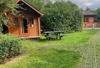Foto de una cabaña de troncos básica en Urban-Gardens Ieper, Bélgica, junto a césped y mesa de picnic.