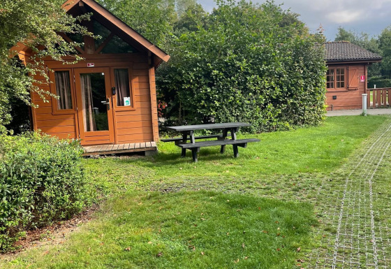 Foto van een Basic log cabin bij Urban-Gardens Ieper, België, met veel groen en een picknickbank buiten.