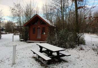 A basic log cabin and a snowy picnic bench at Urban-Gardens Ieper in Belgium during the winter.
