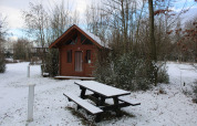 Cabaña básica de troncos y banco de picnic nevado en Urban-Gardens Ieper, Bélgica, en invierno.