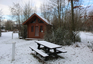 Cabaña básica de troncos y banco de picnic nevado en Urban-Gardens Ieper, Bélgica, en invierno.