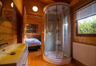 Baño moderno de madera con ducha redonda y ventana en Wellness Lodge del Buitencentrum Hessenheem.