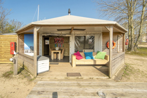 Dune House lodge bij Marina Parcs Almere, Nederland, met houten terras en kleurrijke zitkussens.