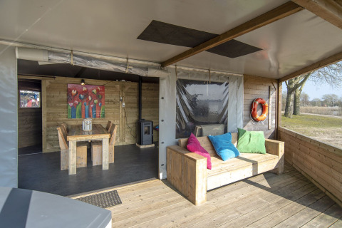 Covered patio of Dune house at Marina Parcs Almere, Netherlands, featuring wooden furniture and bright pillows.