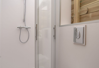 Douche et toilettes modernes au Dune House de Marina Parcs Almere, Pays-Bas, avec mur en bois et porte vitrée.
