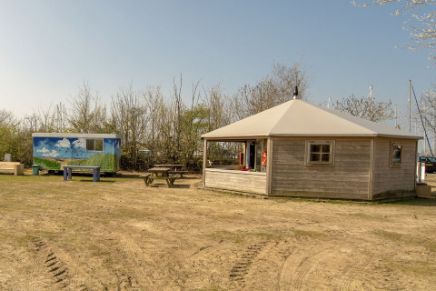 Foto af Dune House-lodgen ved Marina Parcs Almere i Holland med træhytte og picnicborde i forgrunden.
