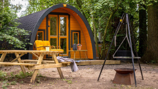 Klein gezellig huisje met gele elementen, picknickbank en vuurkorf bij Buitengoed Ruysbos, Nederland.