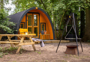 Tiny house accogliente con facciata gialla, panchina all’aperto e braciere a Buitengoed Ruysbos, Paesi Bassi.