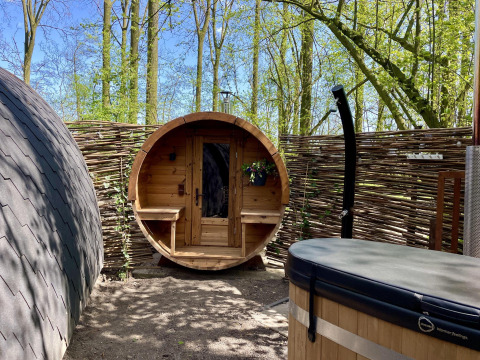 Outdoor wellness area with barrel sauna and hot tub at Boshuys Ultra Wellness tiny house in Buitengoed Ruysbos, Netherlands.