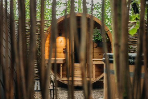 Uitzicht tussen de bomen op een ronde houten hut bij Boshuys Ultra Wellness, Buitengoed Ruysbos, Nederland.