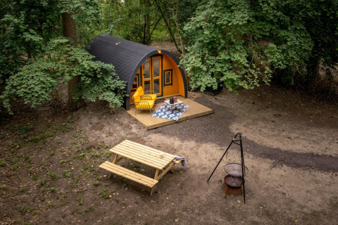 Kleine hut Boshuys Ultra Wellness bij Buitengoed Ruysbos in Nederland, omringd door bomen en tuinmeubilair.