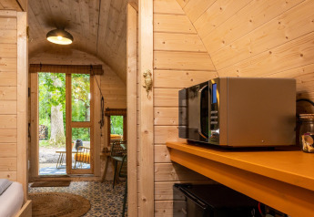 Interior de una tiny house con paredes de madera, microondas y vista al jardín en los Países Bajos.
