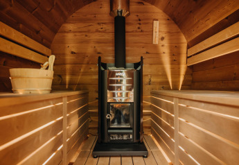 Vista interior de una sauna de madera con estufa y bancos a ambos lados en Boshuys Ultra Wellness, Países Bajos.