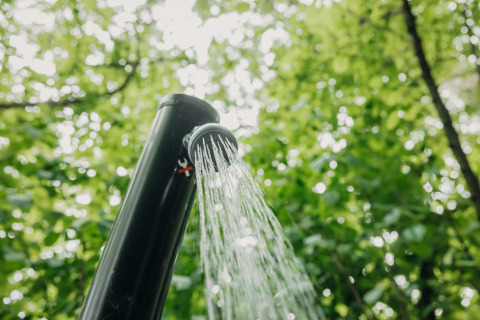 Ducha al aire libre con agua en Boshuys Ultra Wellness, Buitengoed Ruysbos, Países Bajos, rodeado de árboles