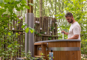 Hombre prepara una bañera de hidromasaje al aire libre rodeada de vegetación en Boshuys Ultra Wellness, Países Bajos.