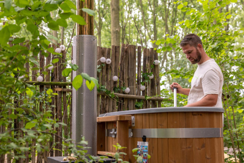 Man prepares outdoor hot tub surrounded by greenery at Boshuys Ultra Wellness in the Netherlands.