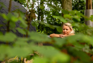Woman relaxing in a wooden hot tub surrounded by greenery at Boshuys Ultra Wellness, Buitengoed Ruysbos, Netherlands.