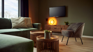 Moderne lodge woonkamer met groene bank, accentstoel, ronde houten tafels, tv en warme sfeerverlichting.