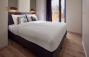 Dormitorio luminoso y moderno de lodge con cama grande, cojines con hojas y vista al exterior por la ventana.