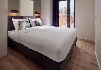 Bright, modern lodge bedroom with large bed, leaf-patterned pillows, wood floor, and window view outside.