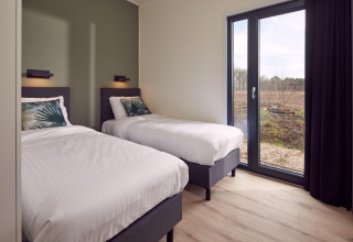 Dormitorio moderno en lodge con dos camas individuales, grandes ventanas y vistas a la naturaleza exterior.