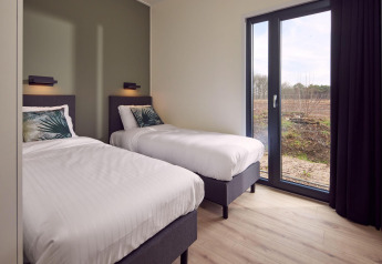 Chambre moderne dans un lodge avec deux lits simples, grandes baies vitrées et vue sur la nature.