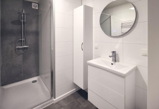 Baño moderno en un lodge con ducha de vidrio, lavabo blanco, espejo redondo y diseño minimalista blanco.
