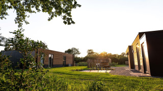 Moderne Ferienvillen bei Sonnenuntergang auf grünem Gelände im Hofparken De Bergvennen, Niederlande.
