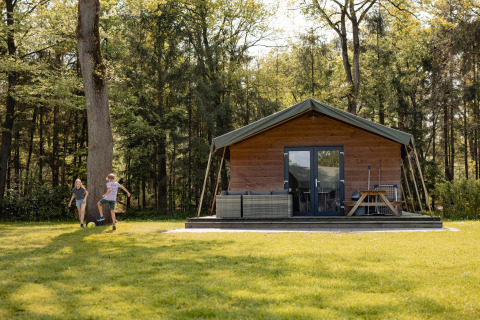 Des enfants jouent devant une tente Safarilodge au Camping the Noetselerberg, aux Pays-Bas, entourés de forêt.