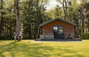Børn leger foran en Safarilodge på Camping de Noetselerberg i Holland med skov i baggrunden.