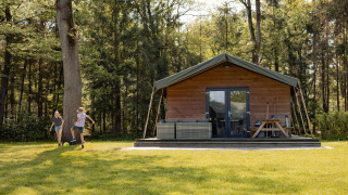 Kinder spielen vor einer Safarilodge auf dem Campingplatz Noetselerberg in den Niederlanden im Grünen.