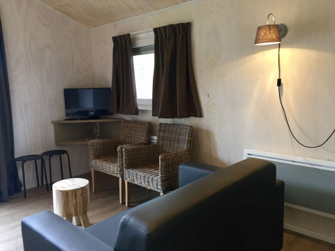 Sala de estar de una tienda Safarilodge en Camping the Noetselerberg con sillas de mimbre y TV.