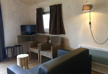 Woonkamer in Safarilodge tent bij Camping de Noetselerberg met rotan stoelen, bank en televisie.