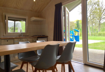 Interieur van Safarilodge op Camping de Noetselerberg, Nederland, met uitzicht op speeltuin door open deur.