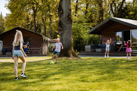 Niños jugando frente a tiendas Safarilodge en Camping the Noetselerberg, Países Bajos, día soleado.