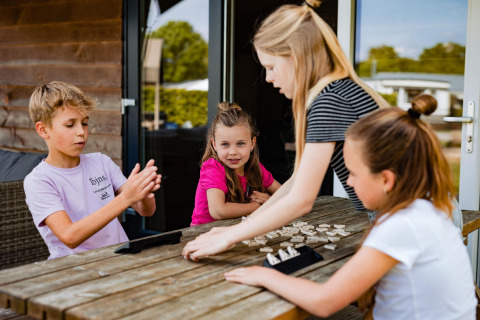 Kinder spielen ein Brettspiel draußen in einem Safarilodge-Zelt auf Campingplatz Noetselerberg, Niederlande.